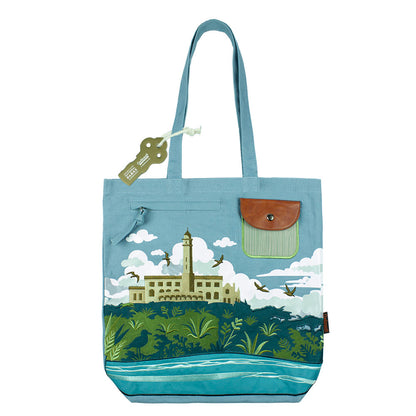 Blue tote bag with an embroidered design of Alcatraz Island, including prison buildings, plants, birds, and fog.