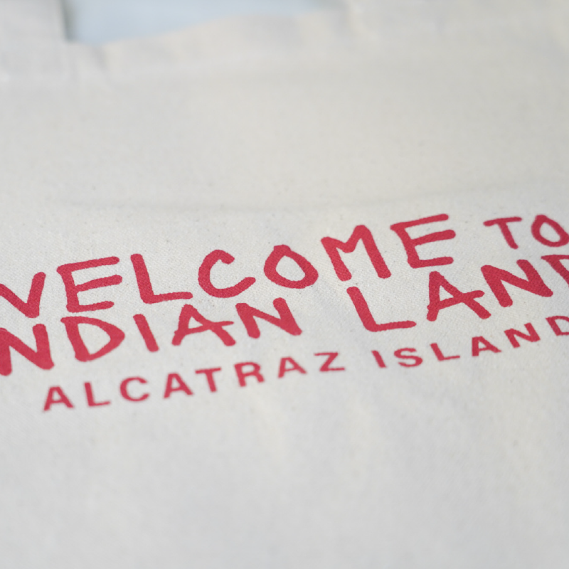 Beige tote bag with red text and Alcatraz Occupation political statements on a white background